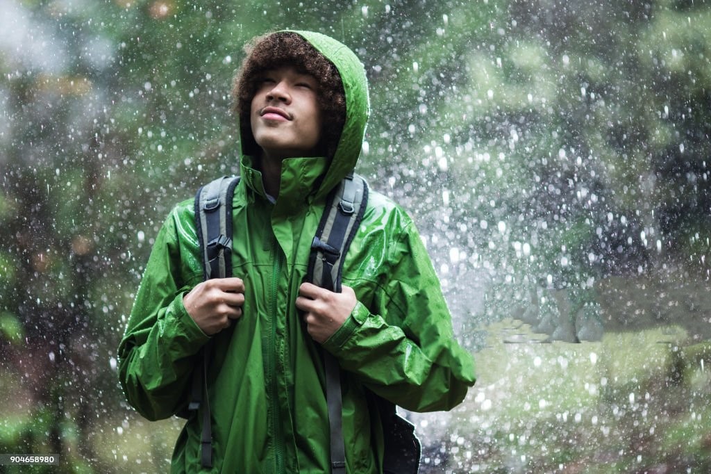 A  man goes for a hike in the rain , the raindrops repelling from his raincoat.